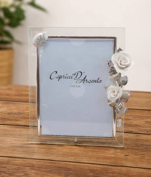 Clear glass photo frame with a silver border and a floral silver-and-white rose embellishment on the right, resting on a wooden table.