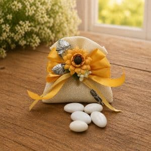 Decorative burlap gift sachet tied with a yellow ribbon and sunflower embellishment on a wooden table with white stones nearby.