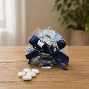 Navy blue ribbon-wrapped wedding favor with silver sailboat accents and white mesh netting on a wooden table.
