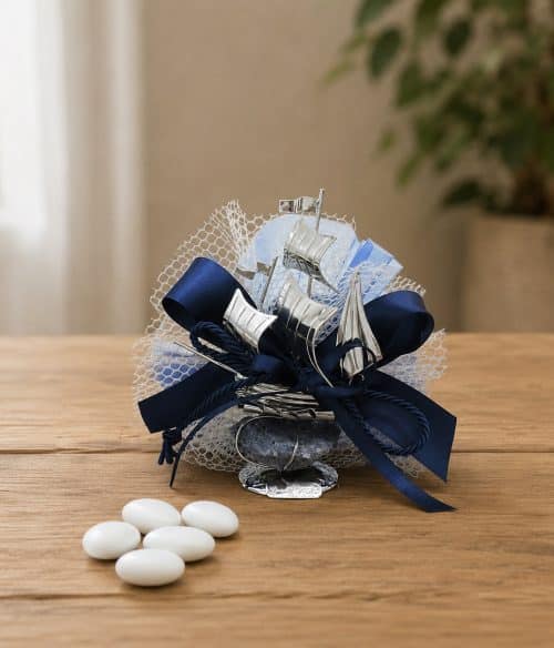 Navy blue ribbon-wrapped wedding favor with silver sailboat accents and white mesh netting on a wooden table.