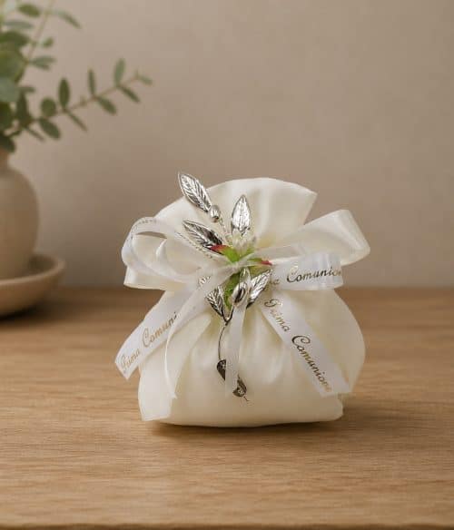 White satin favor bag tied with ribbons and silver leaf charms, a First Communion keepsake on a wooden surface
