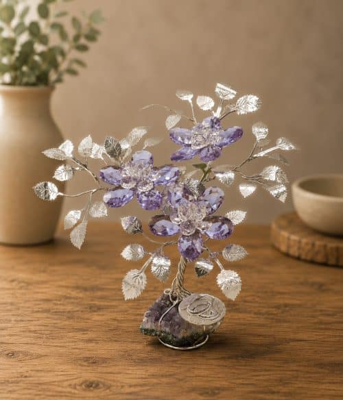 Decorative crystal tree sculpture with purple gem flowers and silver leaves on a wooden table, beige vase blurred in background.