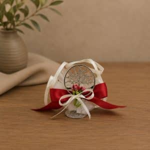 Circular silver ornament with a tree design, wrapped in white and red ribbons on a wooden table