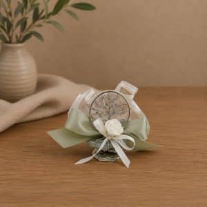 Decorative boutonniere with a silver tree pendant, white rose, and pale ribbons on a wooden table surface.