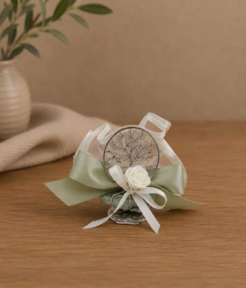Decorative boutonniere with a silver tree pendant, white rose, and pale ribbons on a wooden table surface.