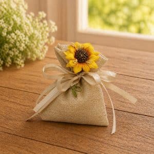 Burlap gift bag with a yellow sunflower and cream ribbon on a wooden table.