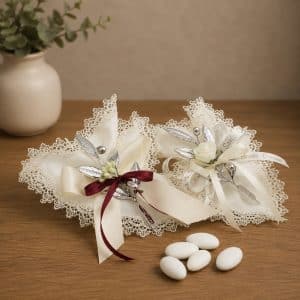 Two lace-edged wedding favors with ivory ribbons, silver leaves, and small white flowers on a wooden table.