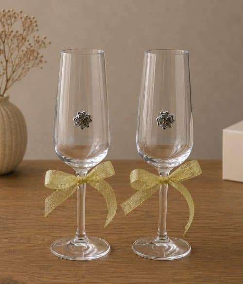 Two champagne flutes with gold ribbons tied around the stems and small '30' emblems, set on a wooden table for a celebration.