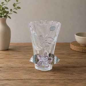 Decorative clear glass vase with flower motifs and purple crystal accents on a wooden table surface.