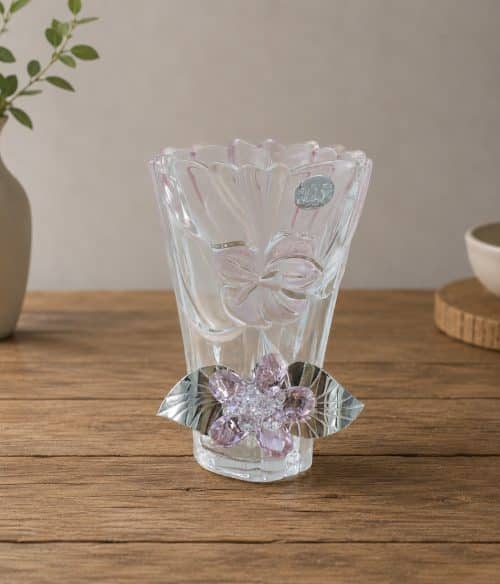 Decorative clear glass vase with flower motifs and purple crystal accents on a wooden table surface.
