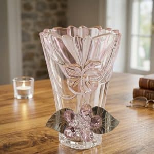 Pink glass vase with a scalloped top and floral detailing, accented by a crystal flower on the bottom, on a wooden table by a candle.