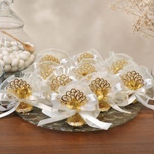 Decorative gold and white wedding favor bows arranged on a glass tray with white candies in a jar nearby.