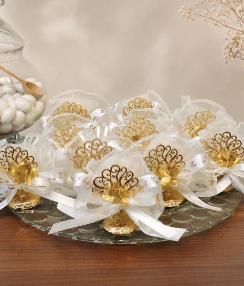 Decorative gold and white wedding favor bows arranged on a glass tray with white candies in a jar nearby.