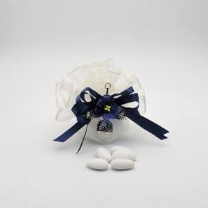 White organza wedding favor pouch with dark blue ribbon bow and blue flower, placed on a white surface with five white almonds nearby.