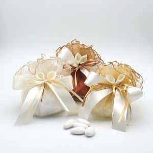 Three decorative wedding favor bags in white and ivory satin with ribbons, arranged with a few white Jordan almonds nearby.